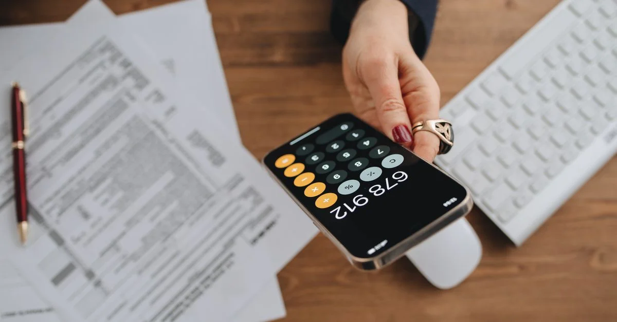 Main tenant une calculatrice smartphone sur des documents fiscaux sur un bureau.