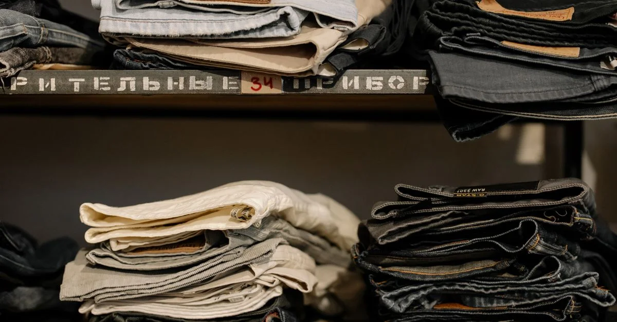 Jeans pliés soigneusement empilés sur des étagères dans un magasin de détail, présentant divers styles et tailles.