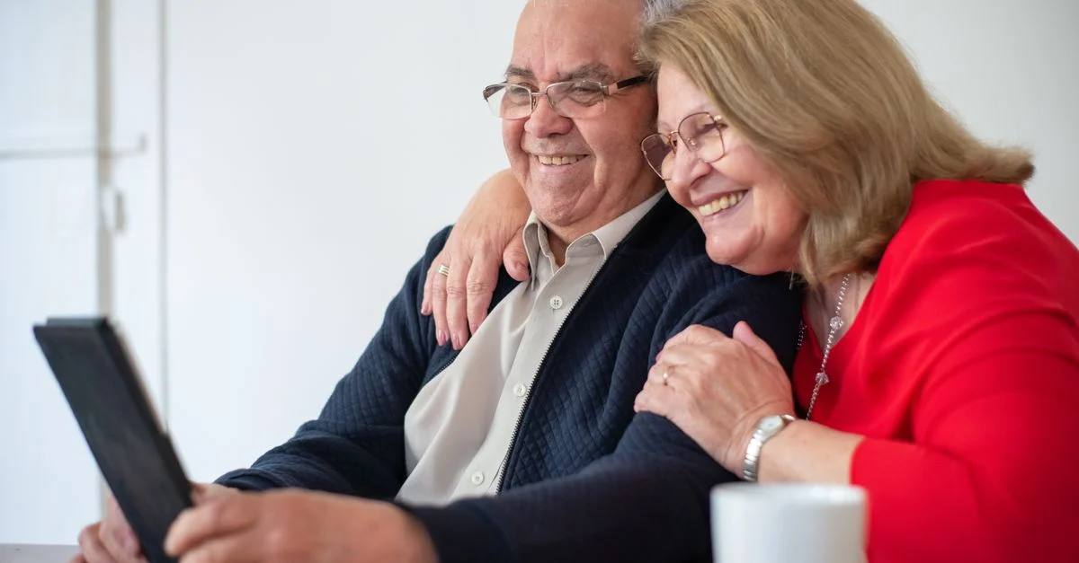 Couple senior heureux s'embrassant tout en utilisant une tablette à l'intérieur. Parfait pour les thèmes de technologie et de style de vie.