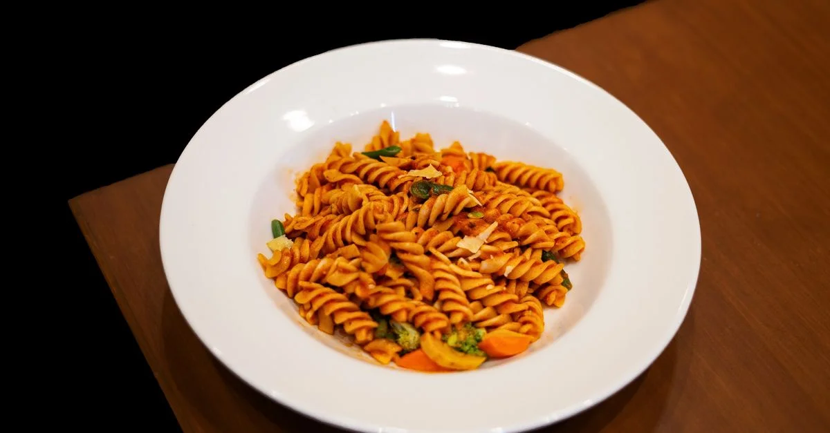 Délicieuse assiette de pâtes fusilli italiennes avec sauce rouge et légumes mélangés sur une table en bois.