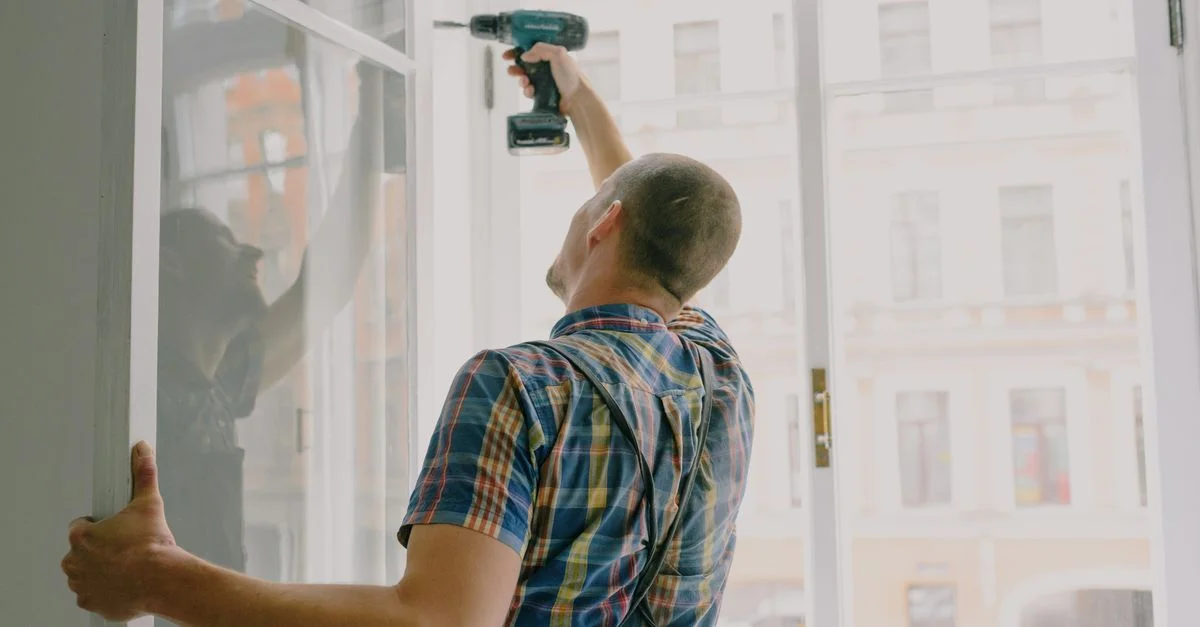 Homme installant une fenêtre à l'intérieur avec une perceuse, concentré sur la rénovation de la maison.