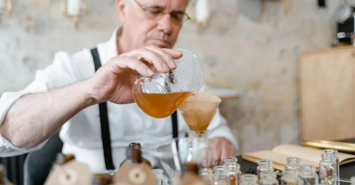 Un homme âgé mélange soigneusement les ingrédients pour créer un parfum dans un atelier chaleureux.
