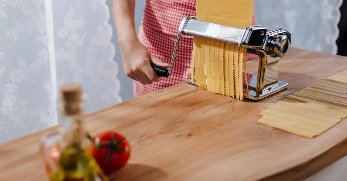 Une femme en tablier rouge utilisant une machine à pâtes pour préparer des pâtes italiennes fraîches.