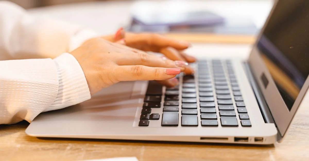 Un gros plan des mains tapant sur un clavier d'ordinateur portable avec un accent sur des ongles manucurés et la technologie.